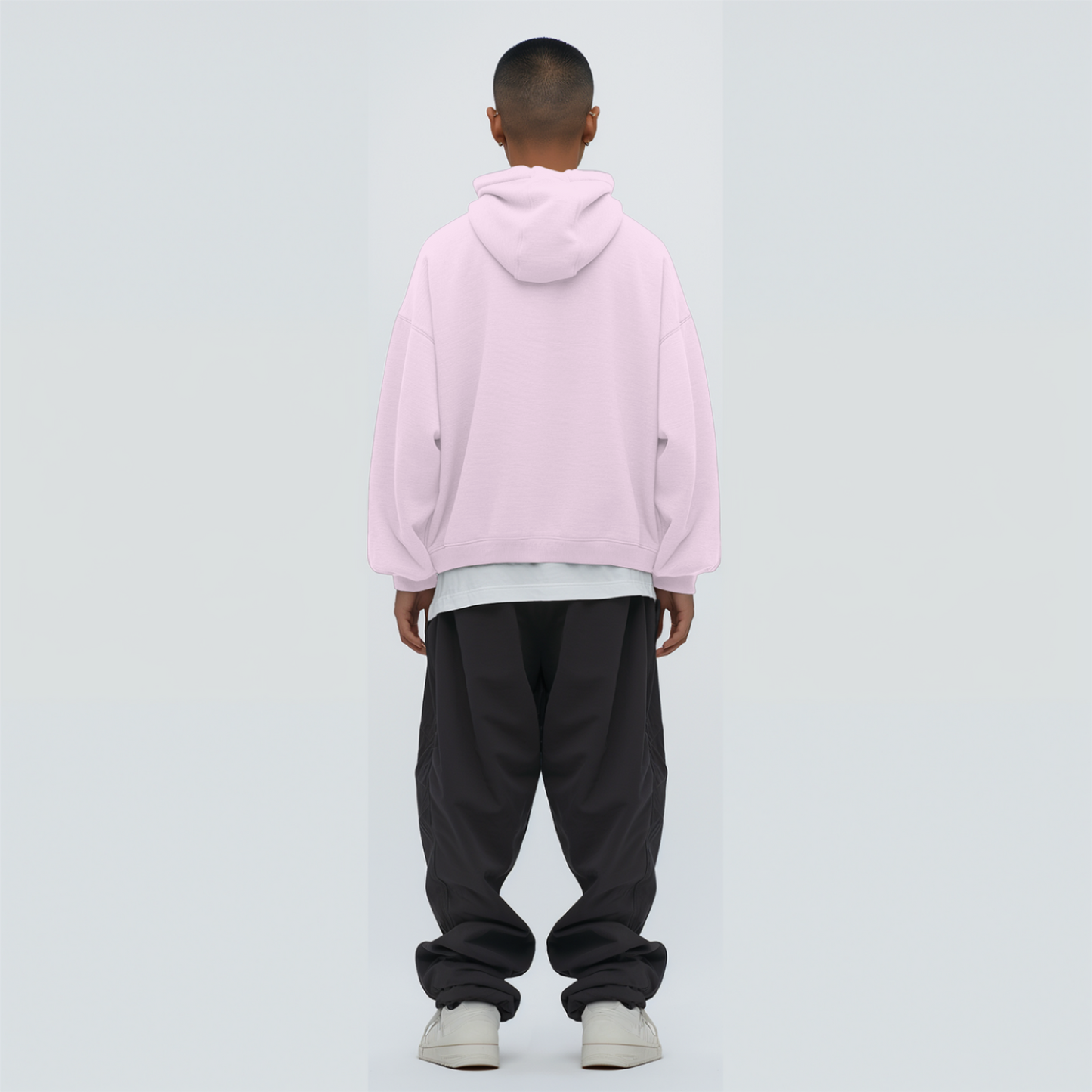 Person wearing a light baby pink hoodie and black pants on a light gray background