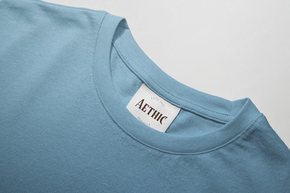 Close-up of a blue t-shirt with 'AETHIC' label on a light gray background