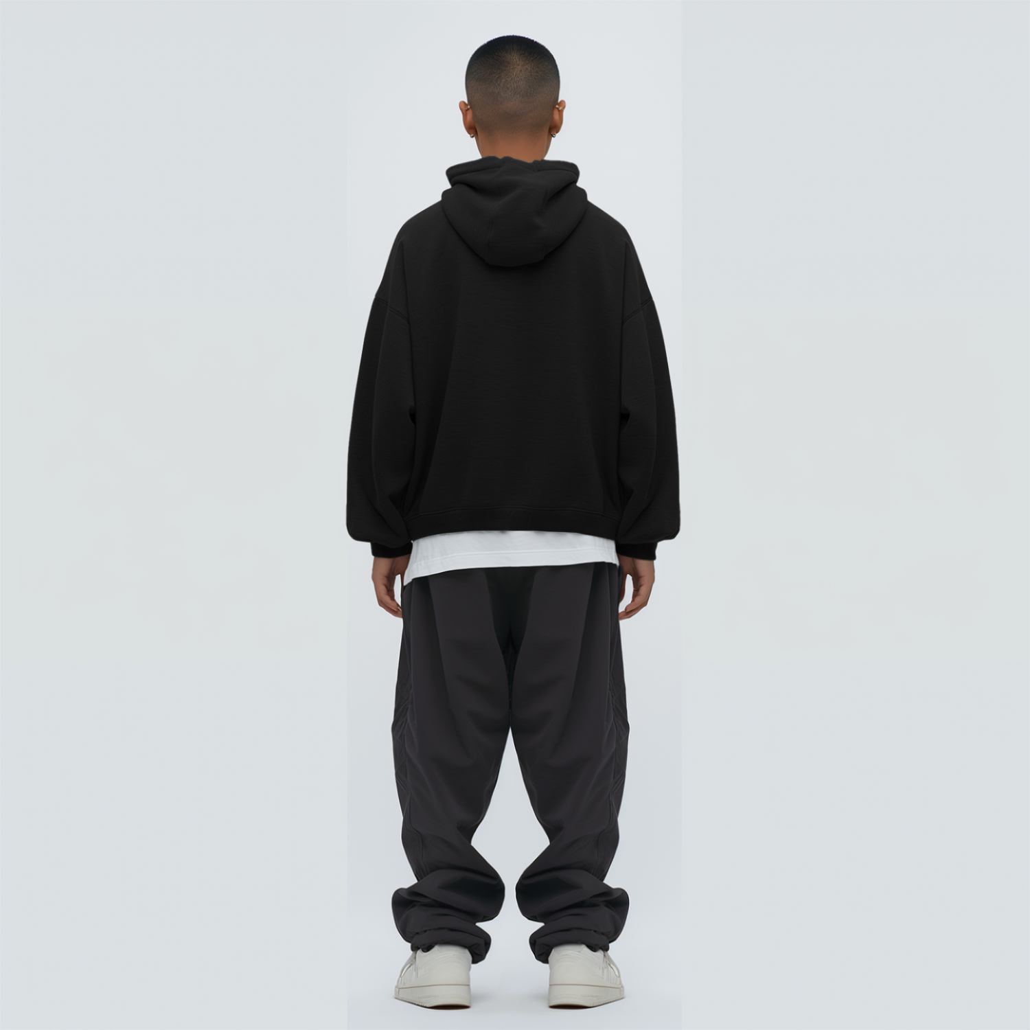 Person wearing a black hoodie and dark pants on a white background