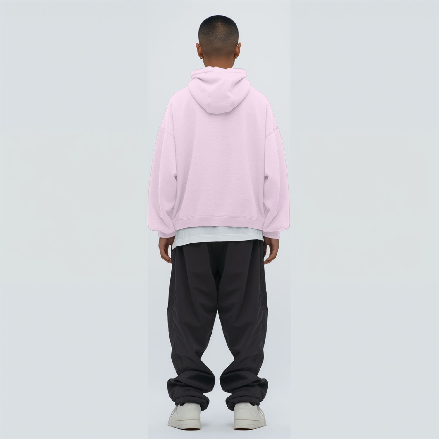 Person wearing a light baby pink hoodie and black pants on a light gray background