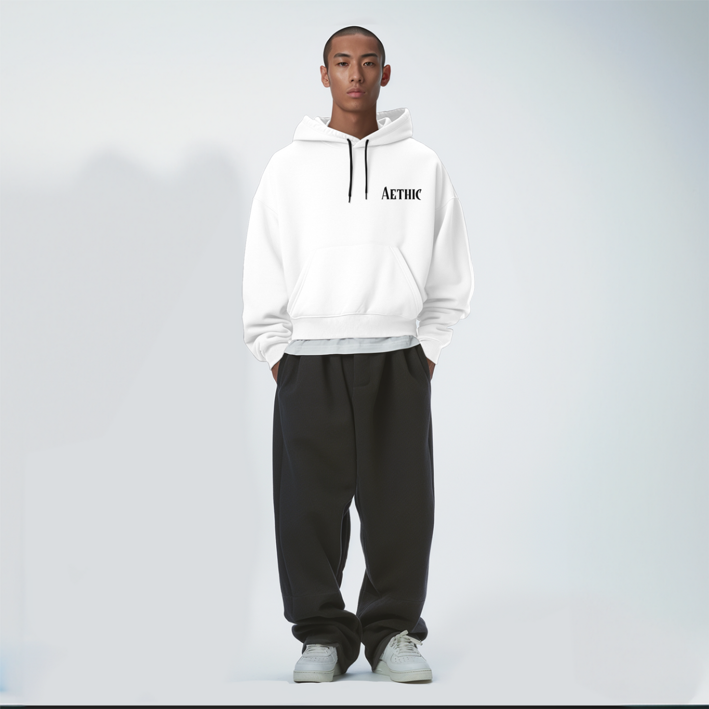 Person wearing a white hoodie with text and black pants on a light gray background