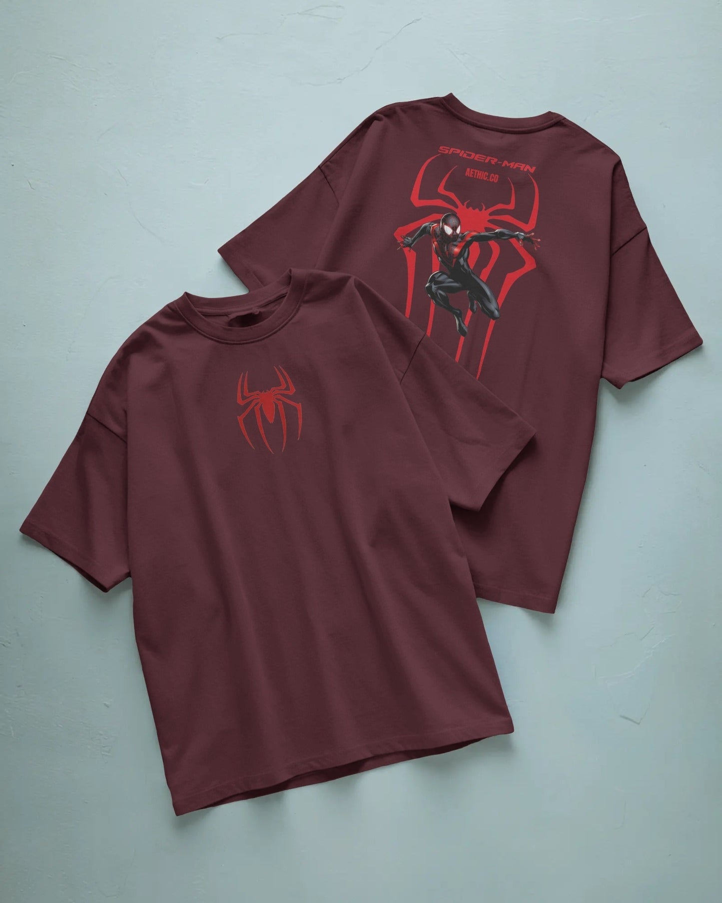 Two maroon t-shirts with spider graphic design on a light blue background