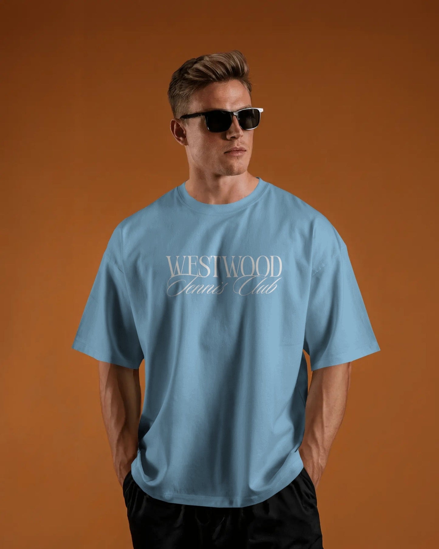 Man wearing a baby blue t-shirt with 'Westwood Club' text on an orange background