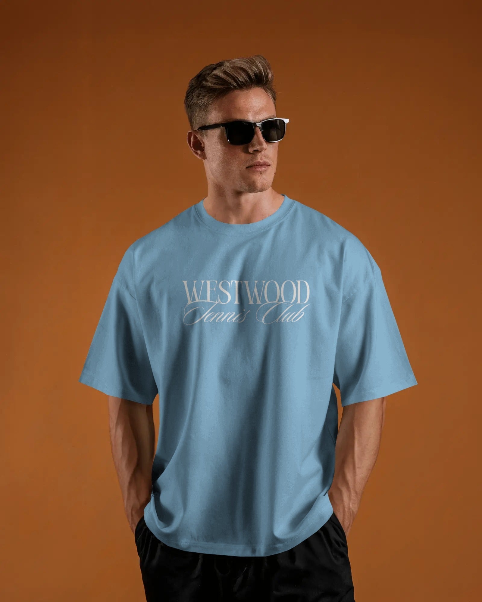 Man wearing a baby blue t-shirt with 'Westwood Club' text on an orange background