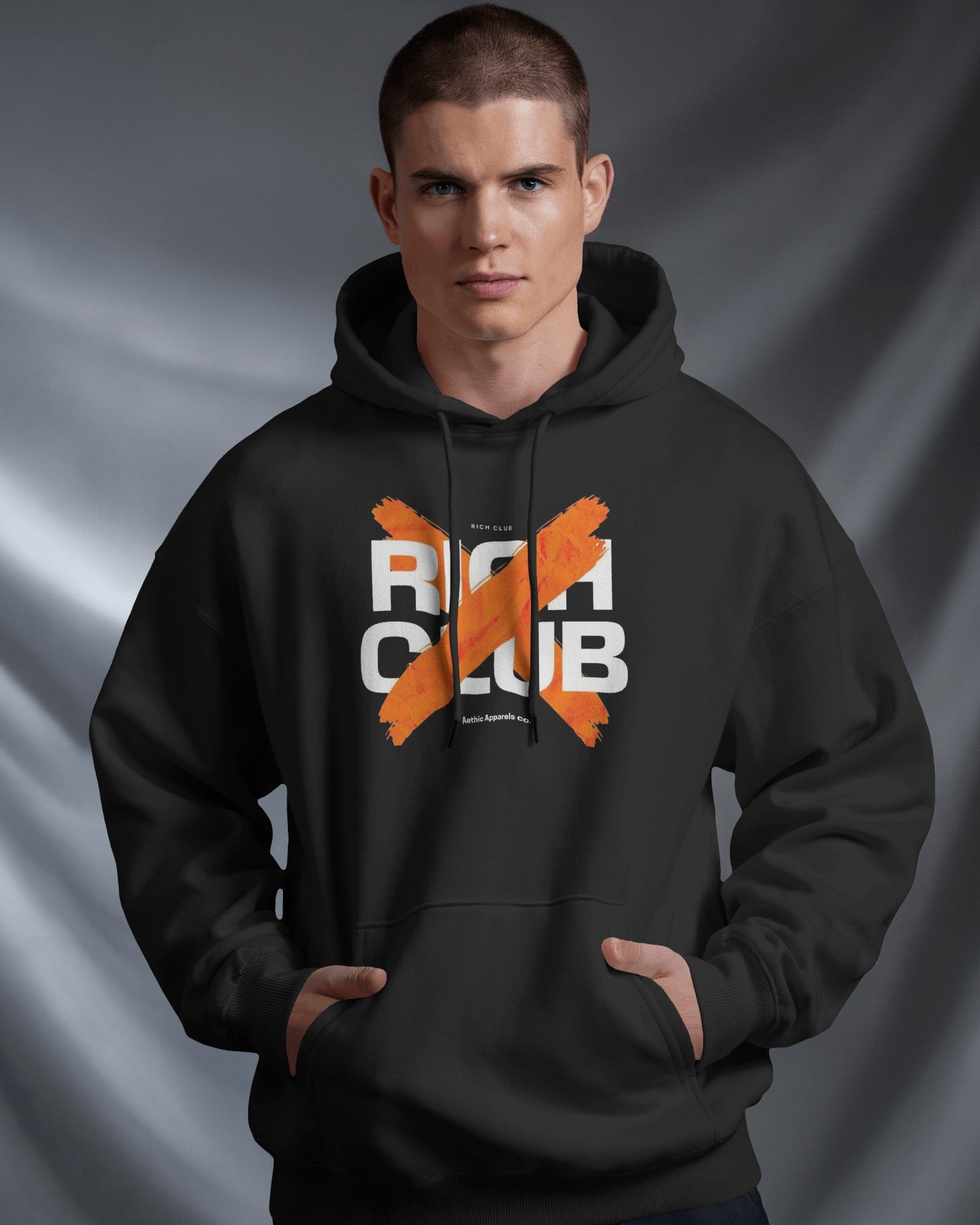 Man wearing a black hoodie with 'RICH CLUB' text and orange design on a gray background