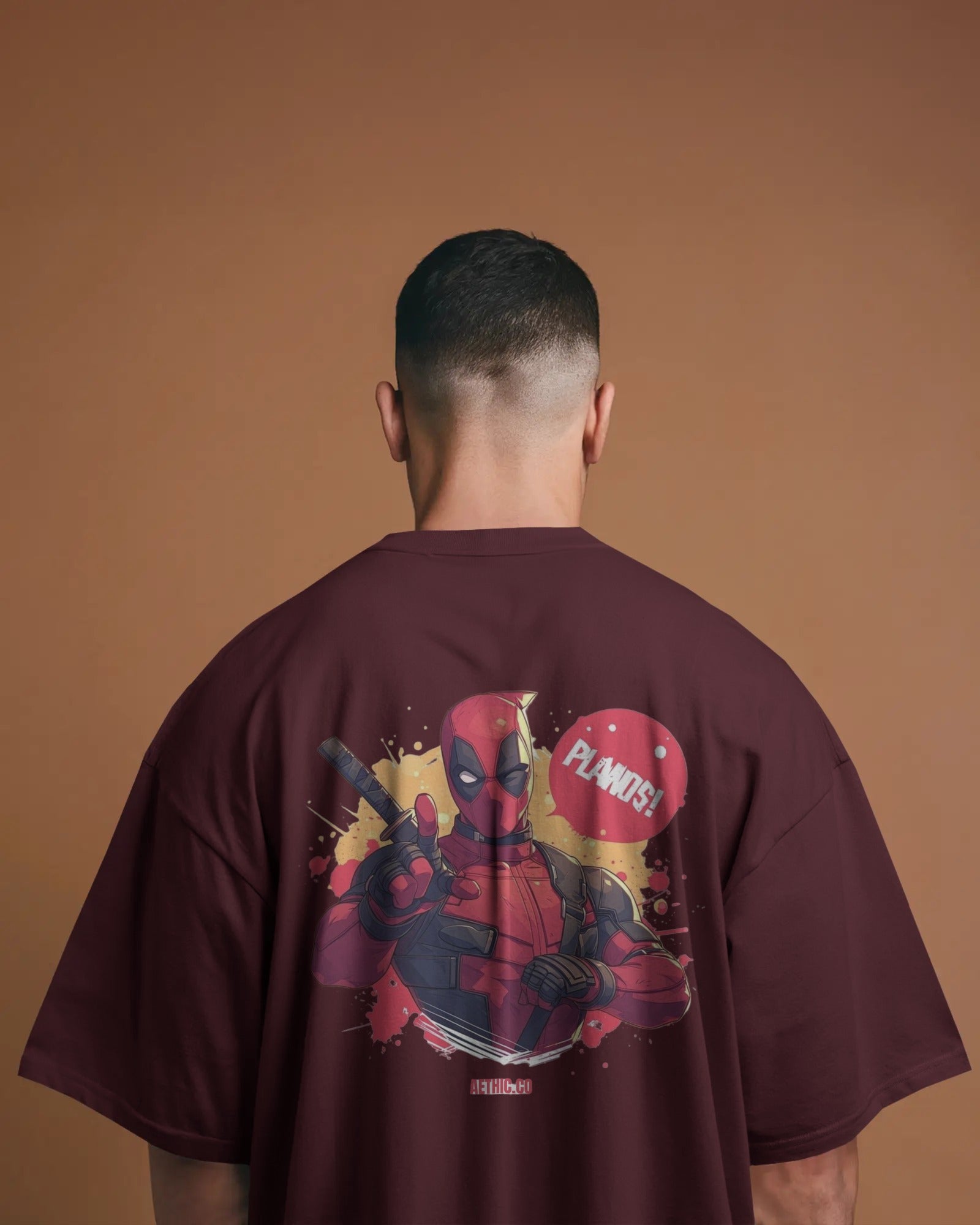 Person wearing a maroon t-shirt with a Deadpool graphic on the back against a brown background