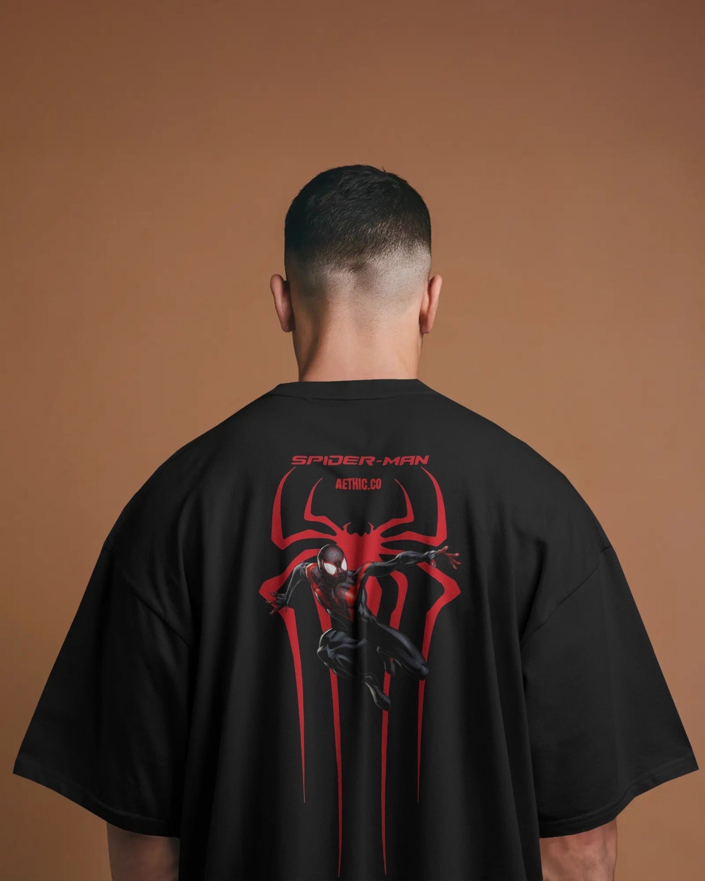 Person wearing a black t-shirt with Spider-Man logo on the back against a brown background