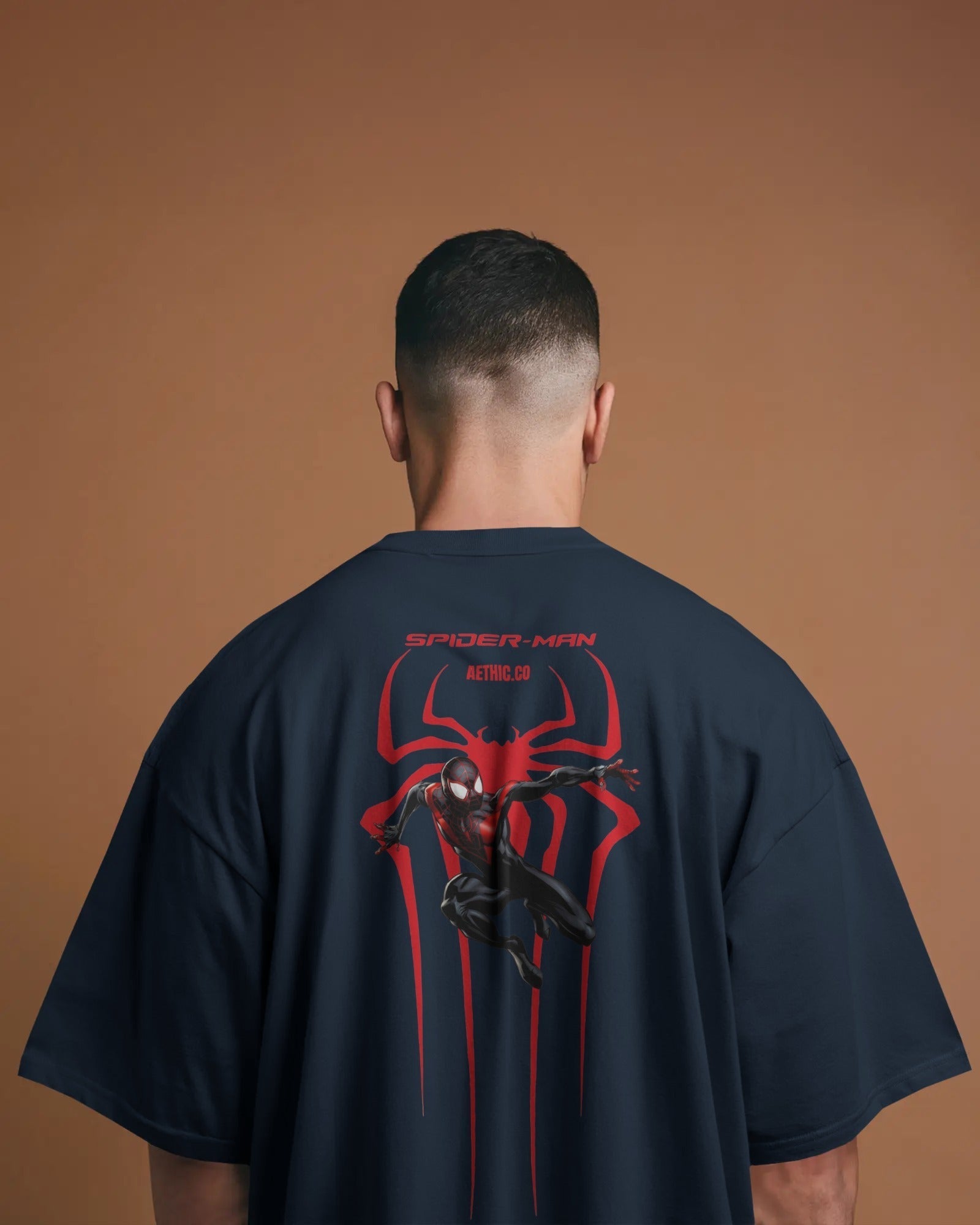 Person wearing a navy blue t-shirt with Spider-Man graphic on the back against a brown background