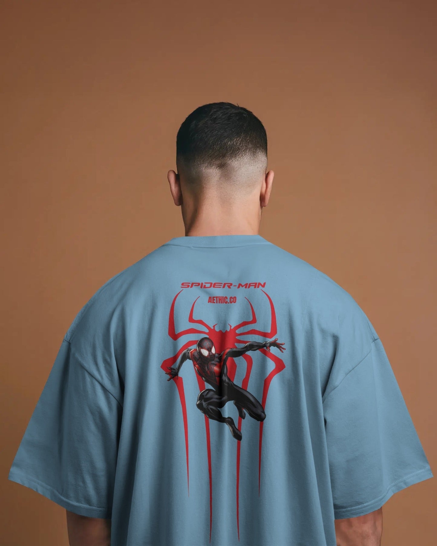 Person wearing a baby blue t-shirt with Spider-Man graphic on the back against a brown background