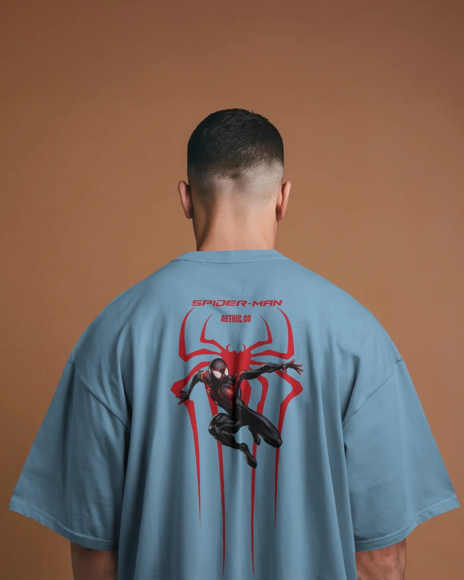Person wearing a baby blue t-shirt with Spider-Man graphic on the back against a brown background