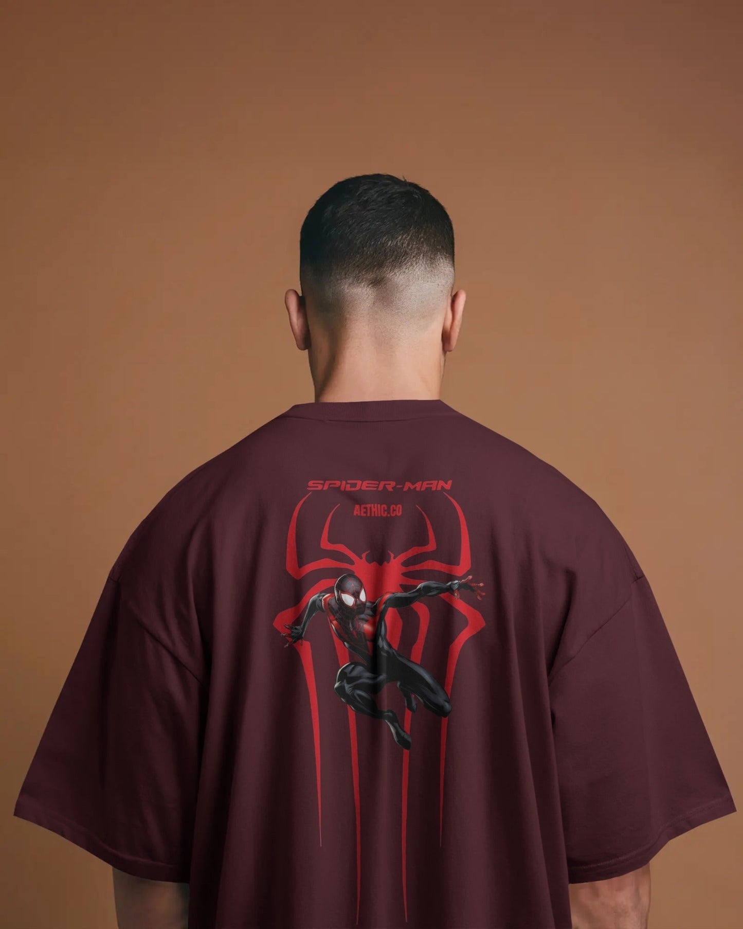 Person wearing a Spider-Man maroon t-shirt with a red and black design on the back against a brown background