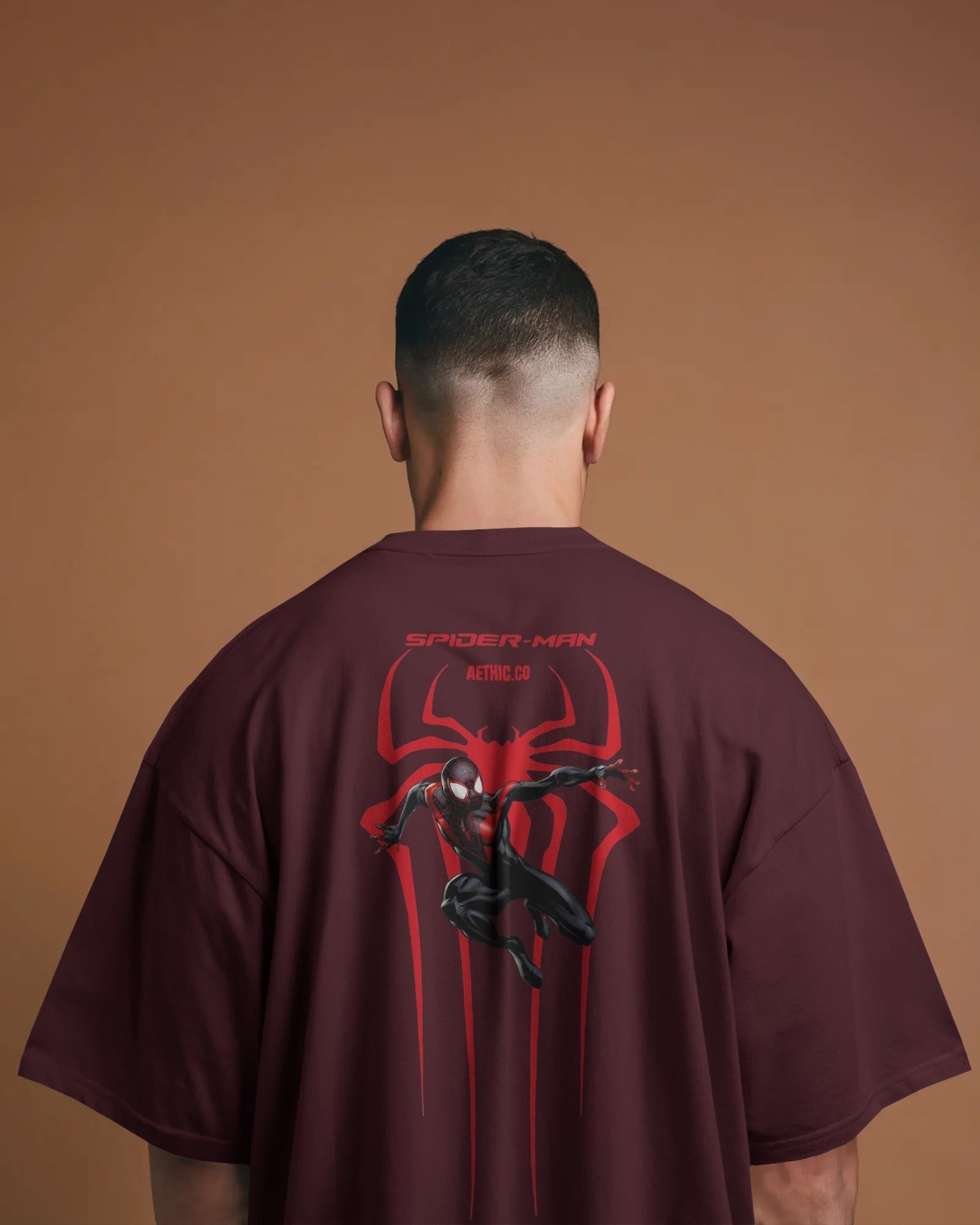 Person wearing a Spider-Man maroon t-shirt with a red and black design on the back against a brown background