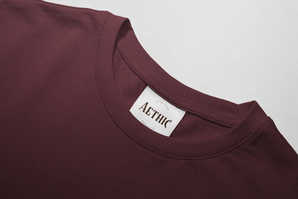 Close-up of a maroon shirt with a 'AETHIC' label on a light gray background