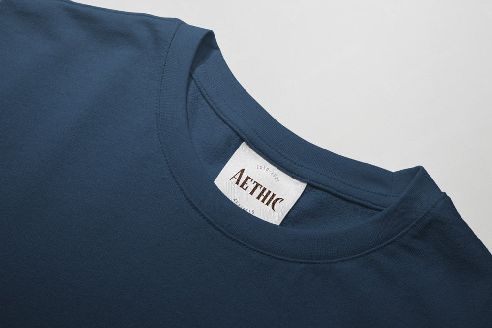 Close-up of a blue t-shirt with a 'AETHIC' label on a light gray background
