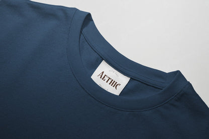 Close-up of a blue t-shirt with a 'AETHIC' label on a light gray background